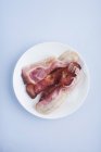 Cooked bacon on round white plate on blue background. — Stock Photo