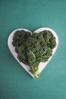 Foglie di cavolo riccio a forma di cuore, Brassica oleracea, in piatto a forma di cuore . — Foto stock