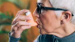 Mujer mayor que usa inhalador de asma con tubo de extensión . - foto de stock