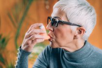 Mulher idosa em uso de inalador de asma com tubo de extensão . — Fotografia de Stock