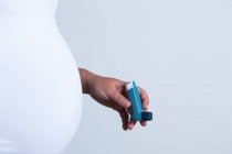 Обрезанное изображение беременной женщины, держащей дыхательные пути от астмы — стоковое фото