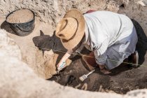 Archaeologist digging with hand trowel, recovering pottery from an archaeological site. — Stock Photo
