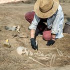 Escavações arqueológicas. Jovem arqueólogo escavando parte do esqueleto humano e crânio do chão. — Fotografia de Stock