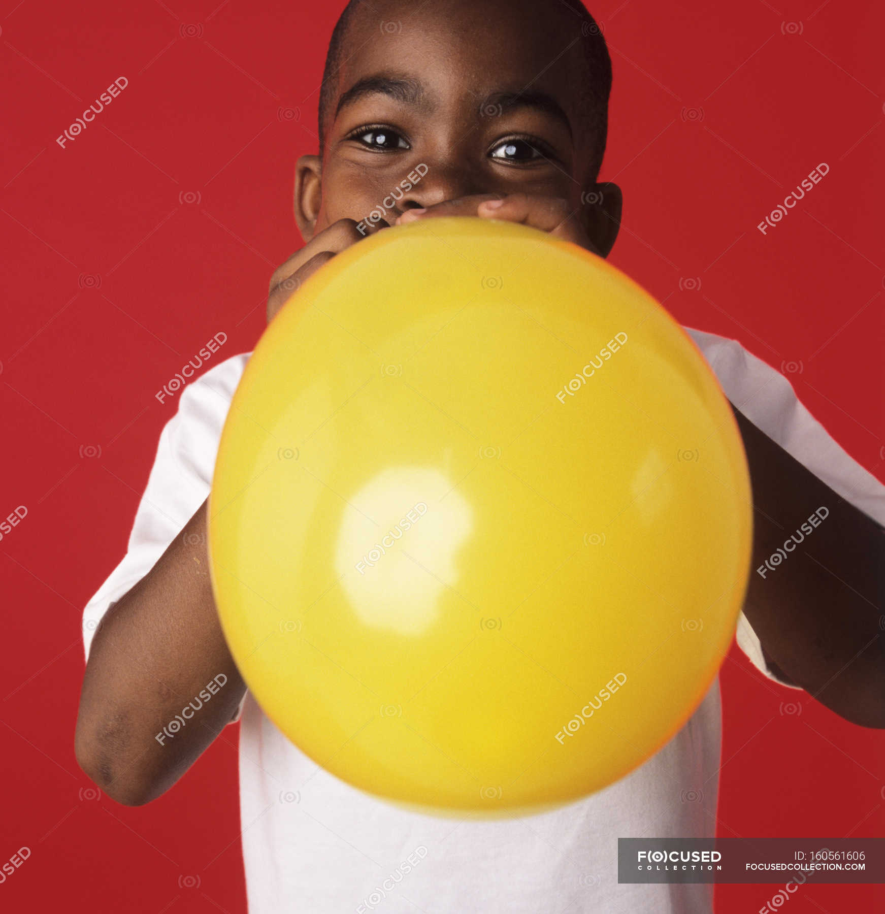 Boy blowing up yellow balloon on red background. — afro caribbean ...