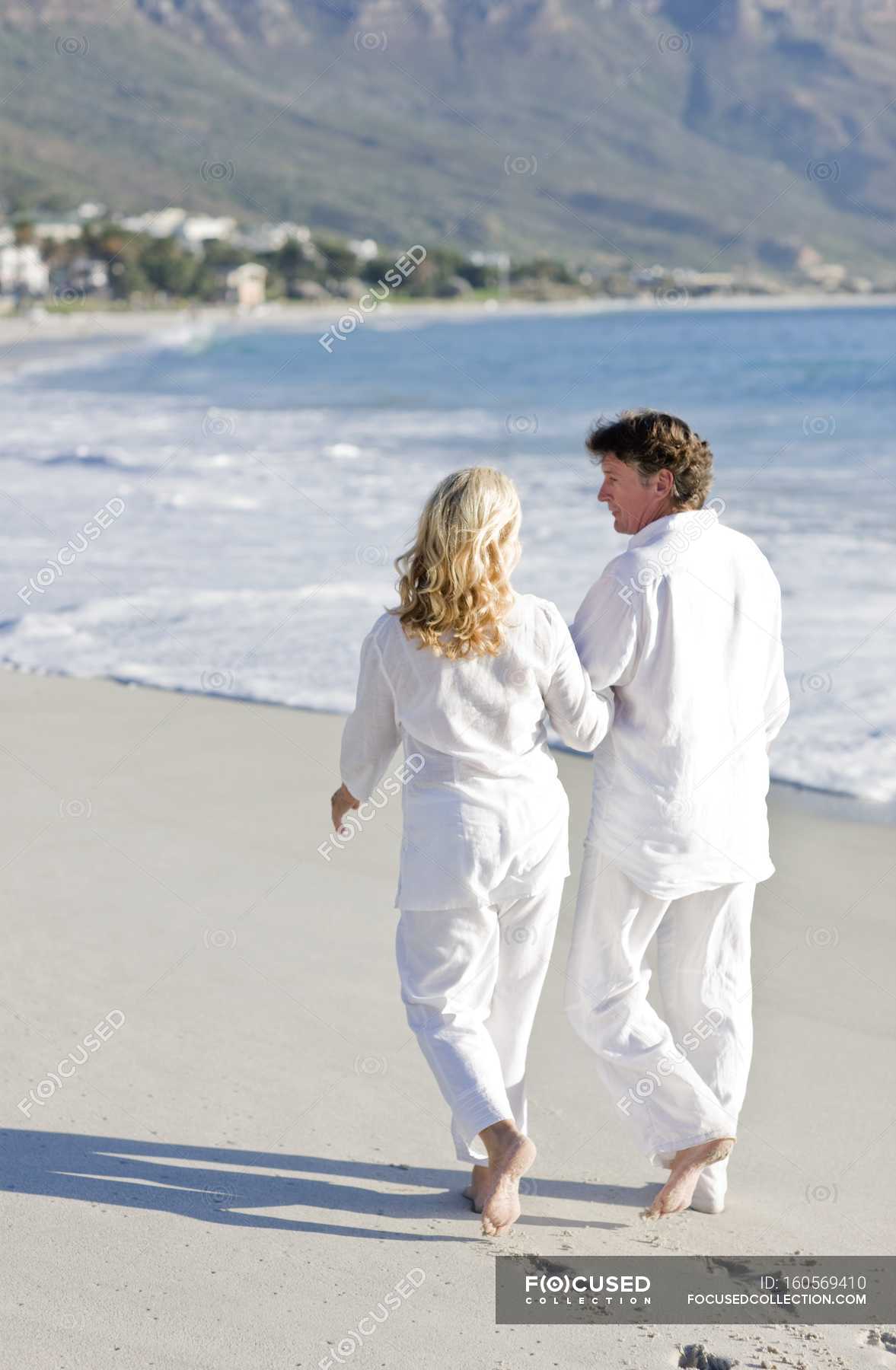 Mature Couple Walking Arm In Arm On Sandy Beach Togetherness Man Stock Photo