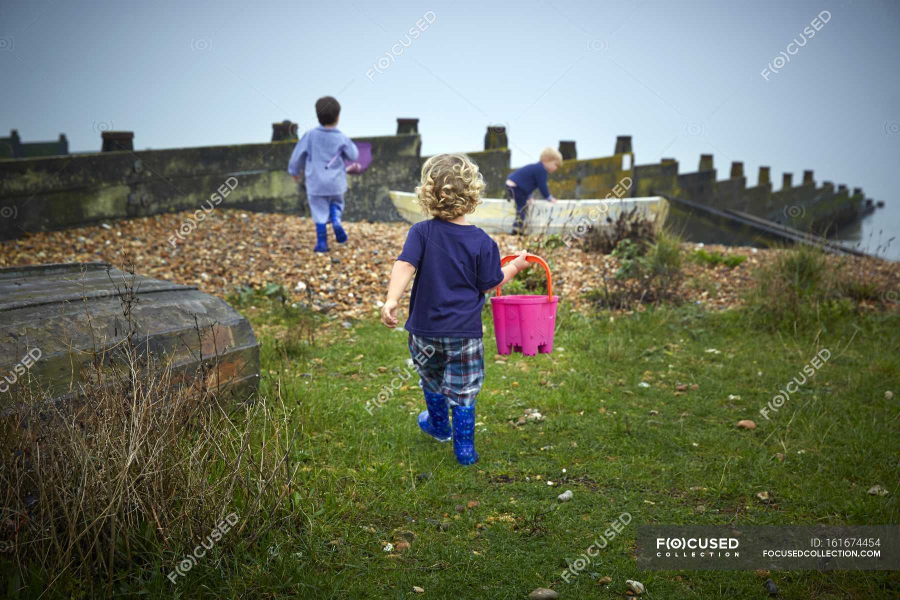 Boy walking with bucket while playing with friends on grassy coastline