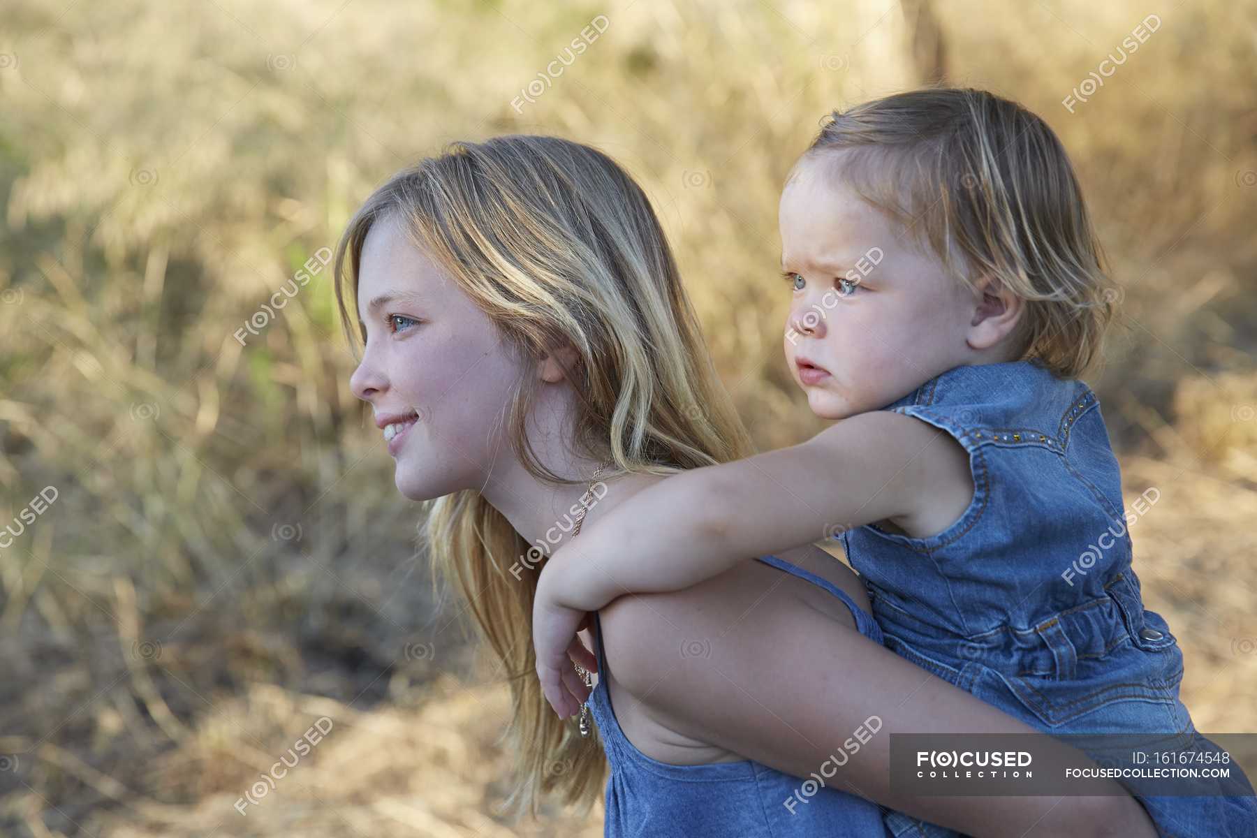 Elementary age girl carrying toddler sister on back. — portrait