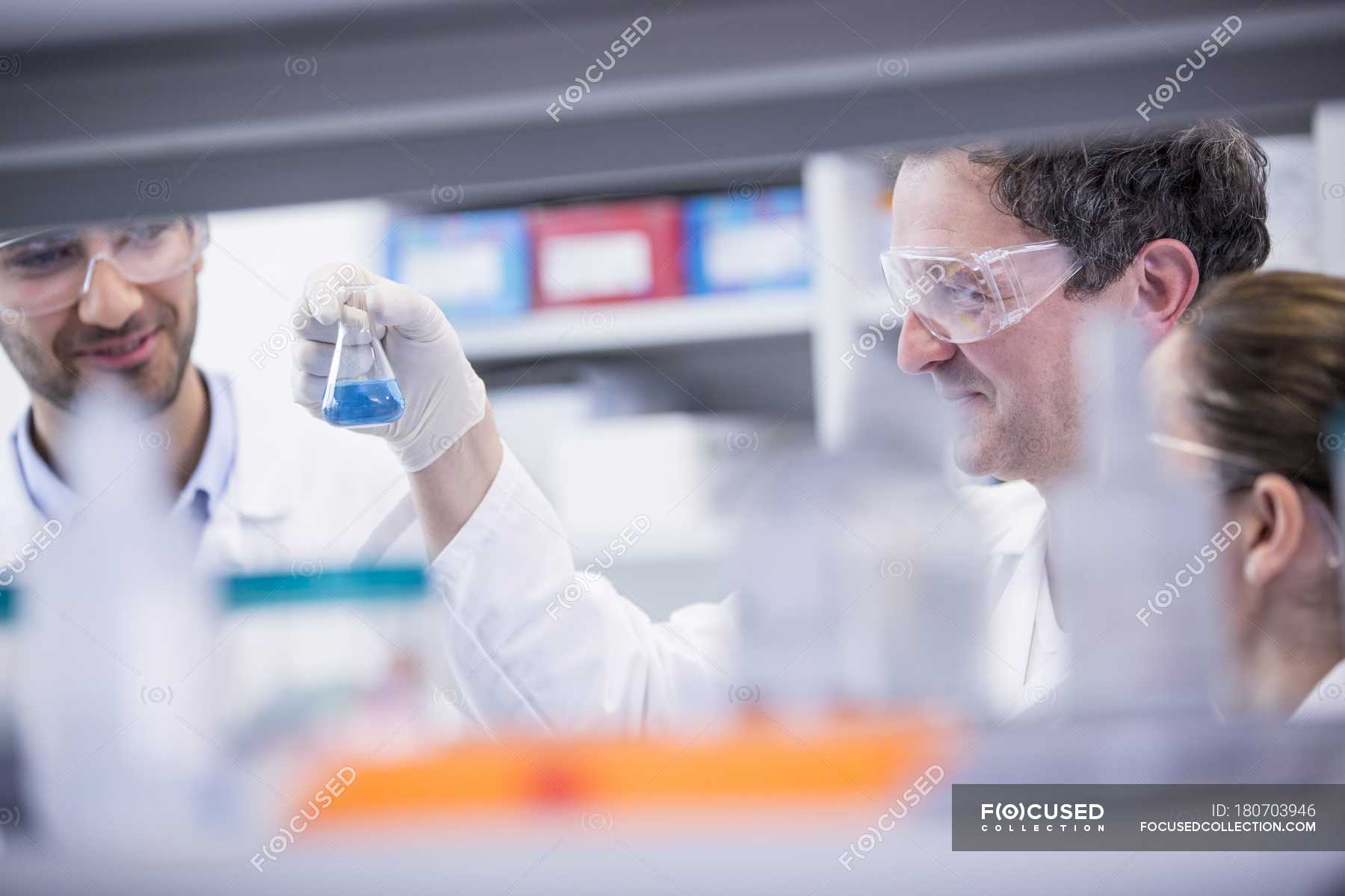 Laboratory assistants looking at chemical flask and smiling. — biology