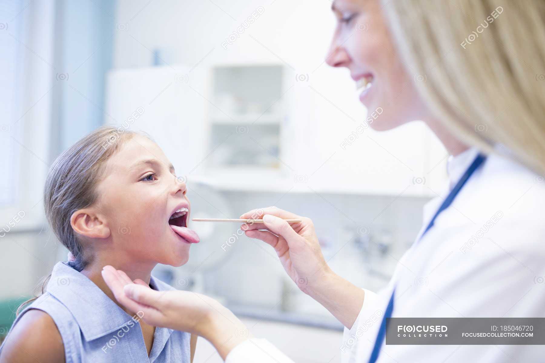 Female doctor examining young girl tongue. — Mouth Open, caucasian