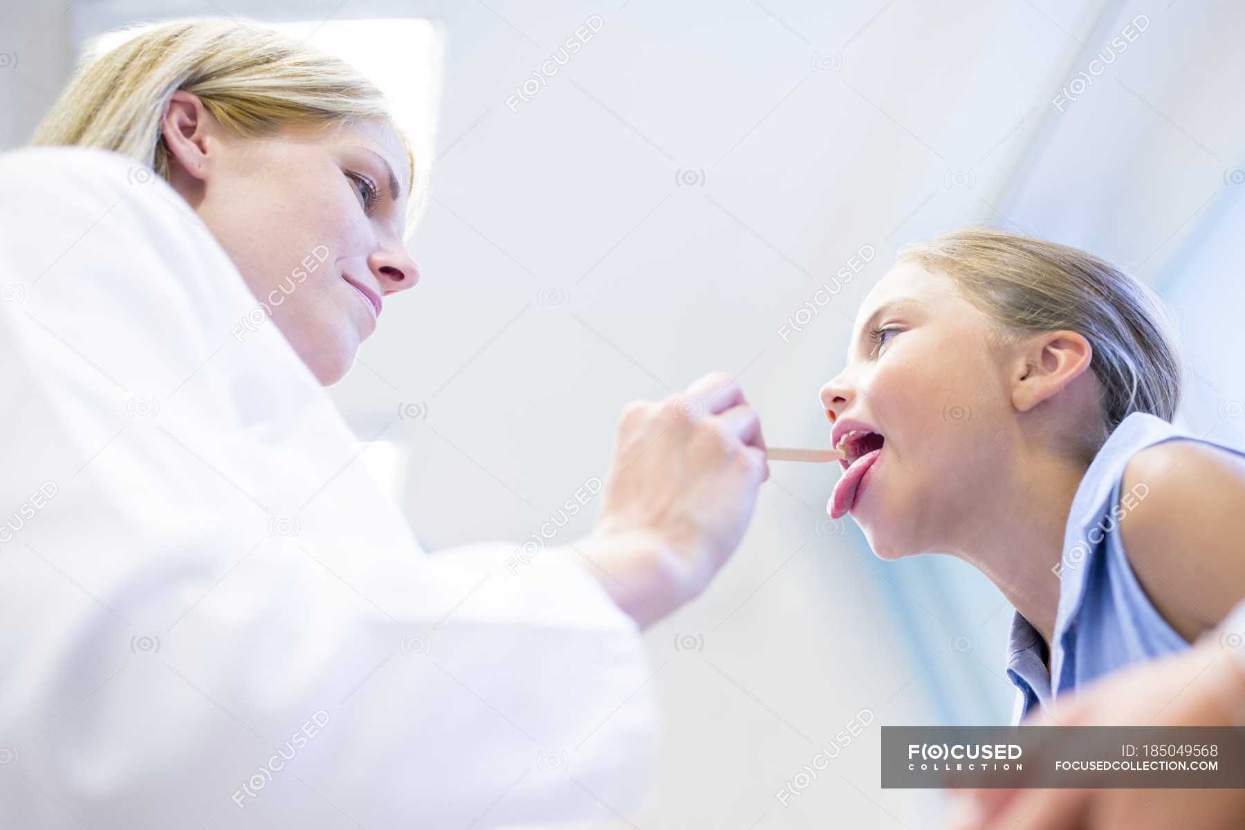 Female doctor examining young girl tongue. — checking, interior Stock