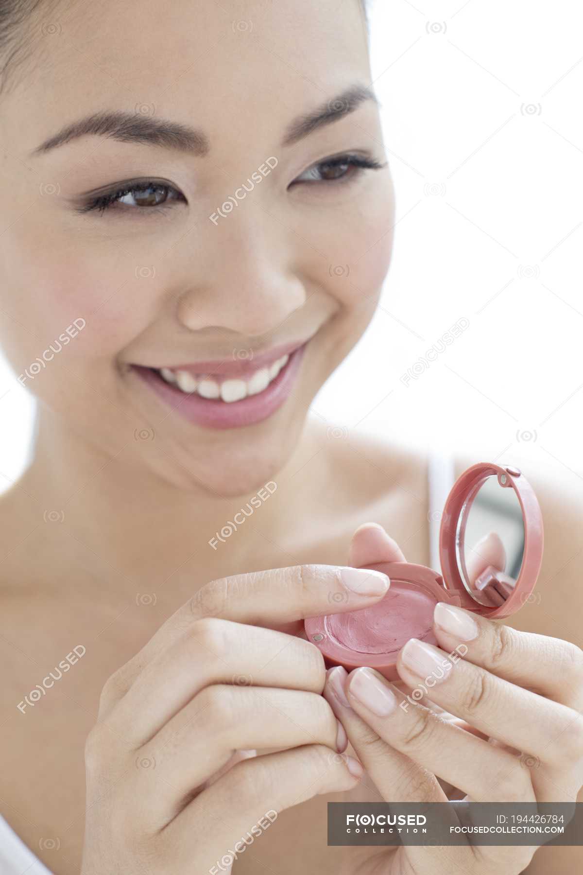 Young Chinese woman applying blusher on white background. — makeup