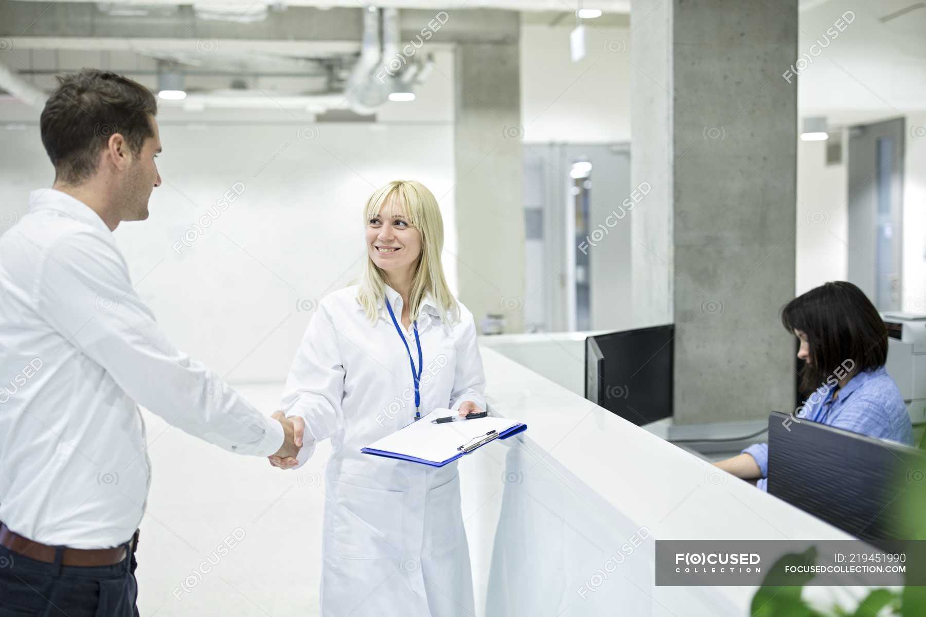 Female Doctor Shaking Hands With Male Patient At Hospital Desk