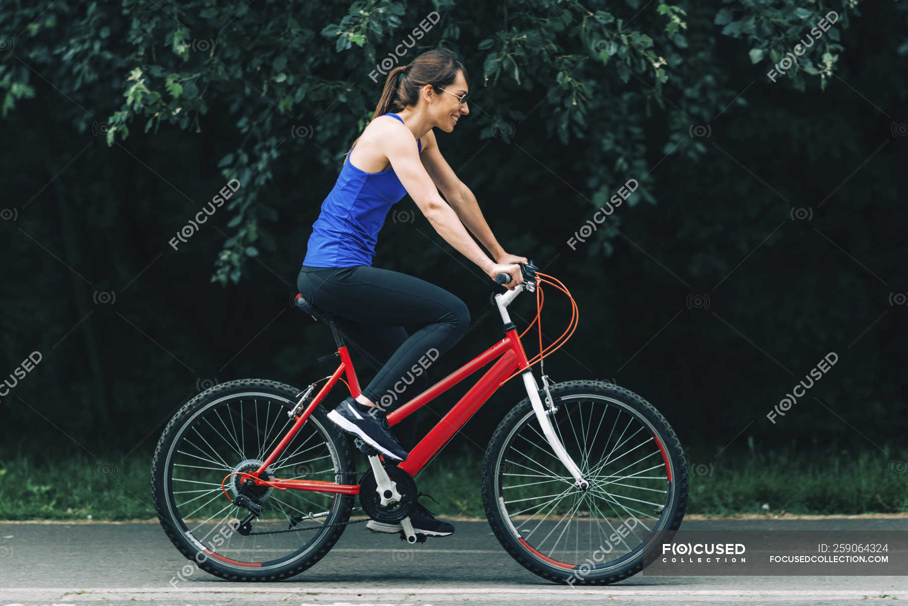 Side view of smiling woman riding bike in park. — fitness, training ...