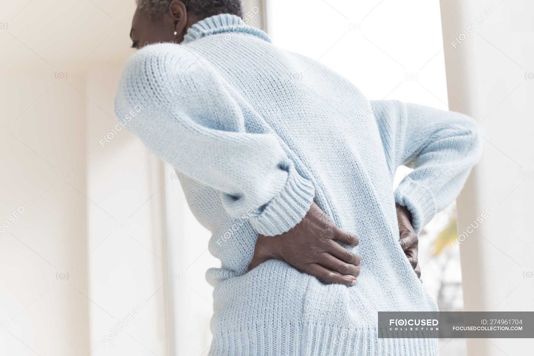 Mature woman with back pain bending forward. — indoors