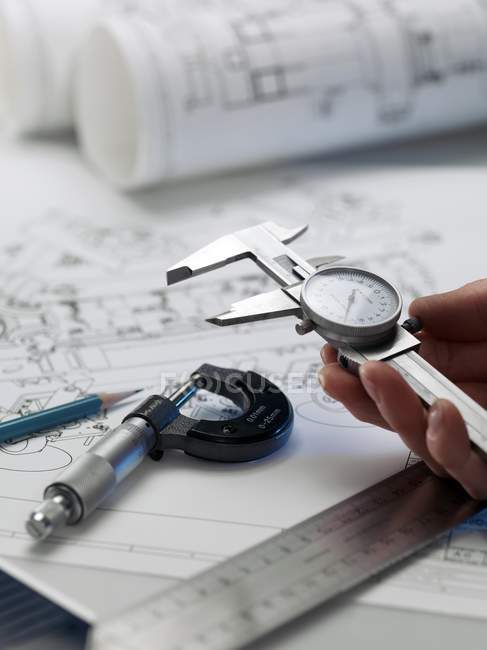Engineer holding dial calipers over blueprints on table. — Stock Photo