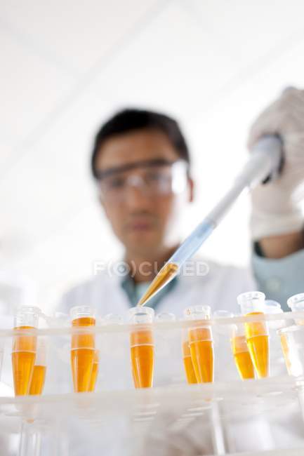 Gros plan d'un scientifique mâle pipettant dans des éprouvettes . — Photo de stock
