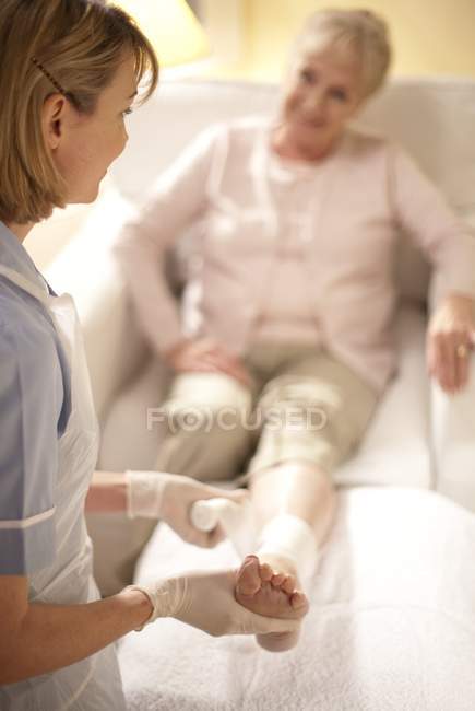 Enfermera ajustando vendaje como tratamiento de úlcera de pierna a paciente mayor . - foto de stock