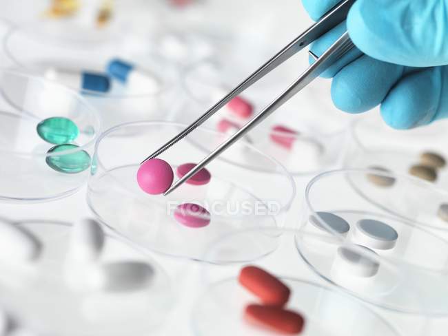 Nahaufnahme einer Person, die eine Pille in der Pinzette hält, für die Pharmaforschung. — Stockfoto