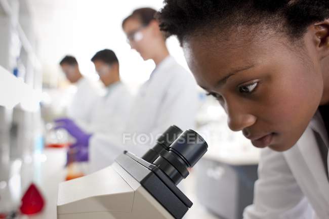 Biologo che lavora con il microscopio con colleghi in background — Foto stock