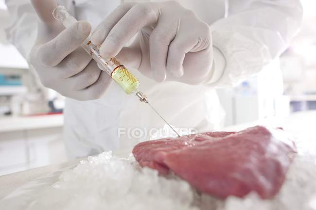 Vue recadrée du scientifique qui injecte de la viande avec une seringue de liquide jaune, image conceptuelle . — Photo de stock