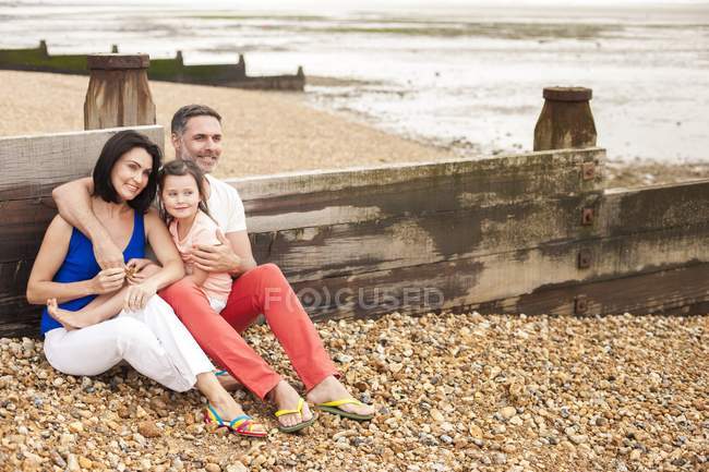 Parents leaning on beach fence with daughter. — Stock Photo