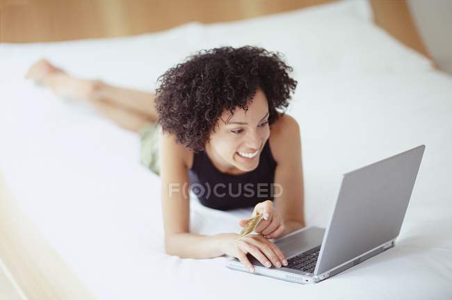 Donna sdraiata sul davanti sul letto e utilizzando il computer portatile . — Foto stock