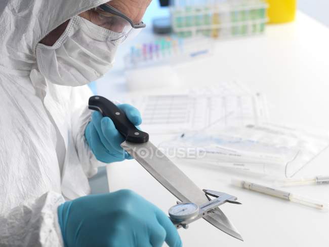 Científico forense midiendo hoja de cuchillo como evidencia forense
. - foto de stock