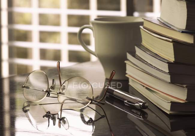 Verres sur table avec tasse, stylo et pile de livres . — Photo de stock