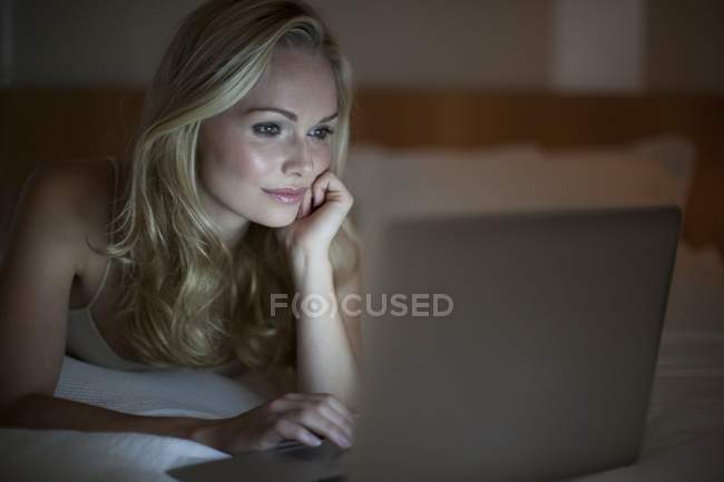 Молодая женщина использует ноутбук с рукой на подбородке . — стоковое фото