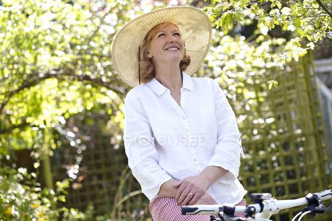 Mulher madura em sunhat ciclismo no jardim . — Fotografia de Stock