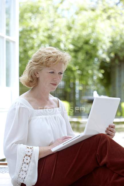 Зріла жінка використовує ноутбук в саду . — стокове фото
