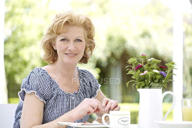 Ältere Frau frühstückt im Garten. — Stockfoto
