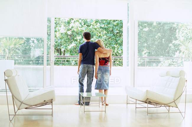 Vista posteriore della giovane coppia guardando la vista attraverso balcone appartamento . — Foto stock