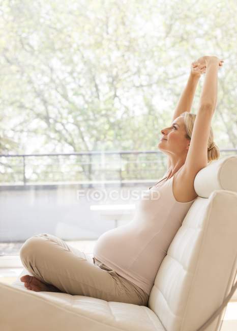 Pregnant woman stretching on sofa — Stock Photo