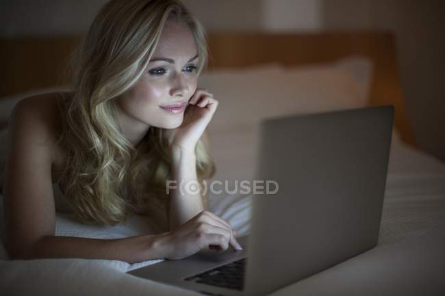 Jovem mulher usando laptop na cama. — Fotografia de Stock