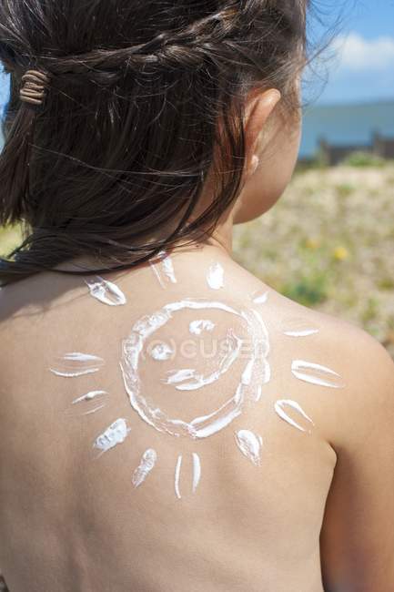 Rear view of girl with sun cream on back in shape of sun. — Stock Photo