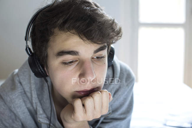 Young man using headphones with hand on chin. — Stock Photo
