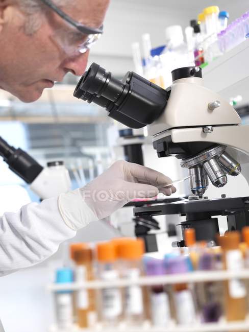 Científico masculino haciendo pruebas médicas de la muestra bajo el microscopio . - foto de stock
