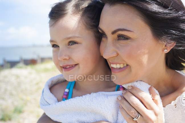 Mother and daughter in towel smiling and looking away on beach, portrait. — Stock Photo