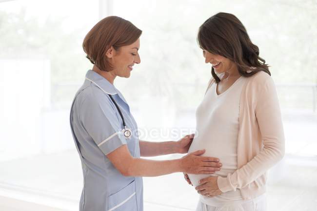 Женщина-медсестра держит беременную женщину животом . — стоковое фото
