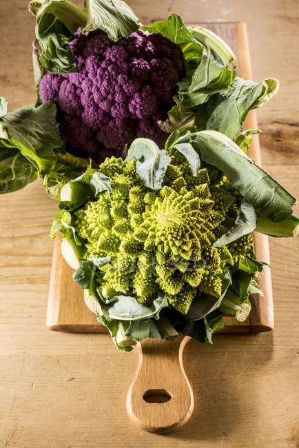 Purple and romanesco cauliflowers on chopping board. — Stock Photo