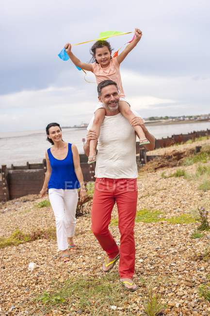 Батько носить дочку на плечах на пляжі з матір'ю . — стокове фото