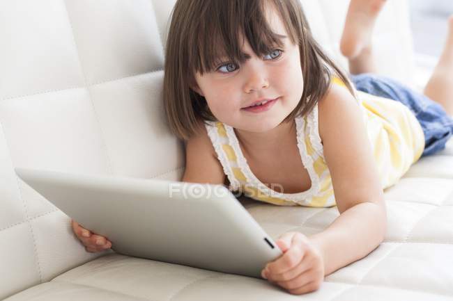 Toddler girl using digital tablet on sofa. — Stock Photo