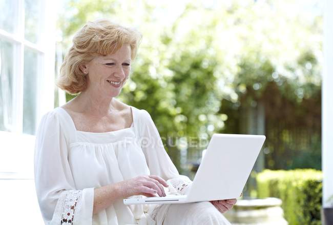 Ältere Frau benutzt Laptop im Garten. — Stockfoto