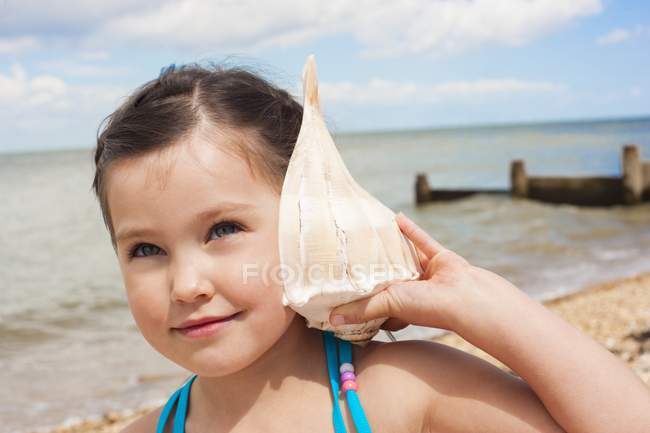 Jeune fille écoute coquillage sur la plage . — Photo de stock