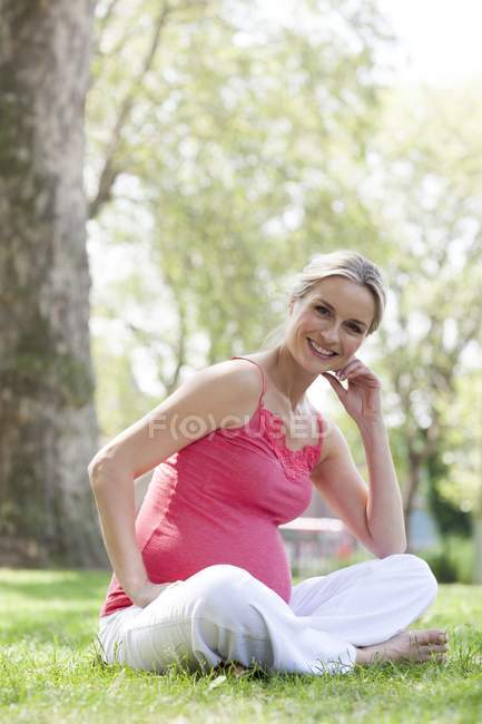Mujer embarazada sentada en la hierba - foto de stock