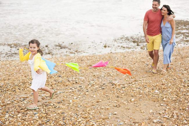 Parents walking on beach with daughter holding bunting. — Stock Photo