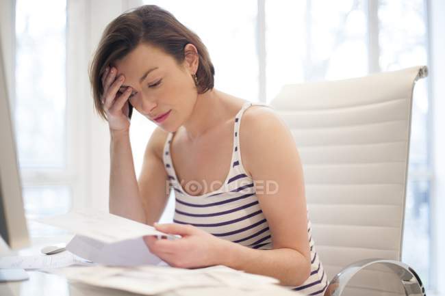 Gestresste Frau schaut auf Rechnungen herab. — Stockfoto