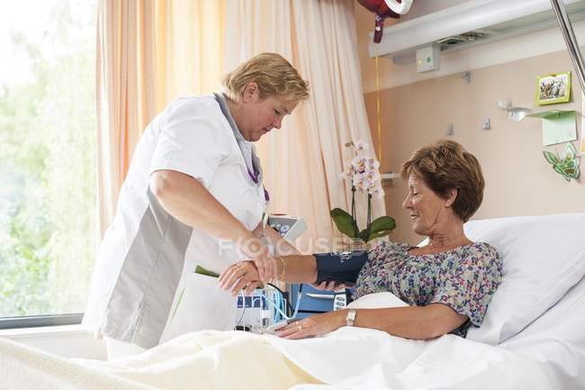 Enfermera midiendo la presión arterial del paciente mayor . - foto de stock
