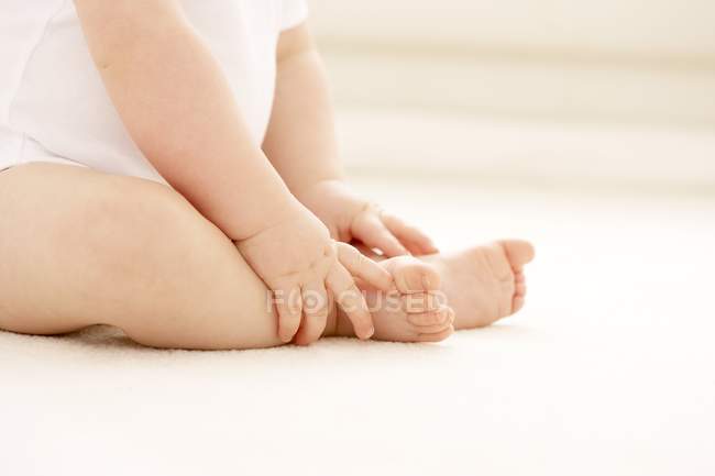 Ребенок держится за ноги, сидя на полу . — стоковое фото